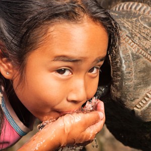 Young Nepali girl drinking from city fountain on Durbar Square